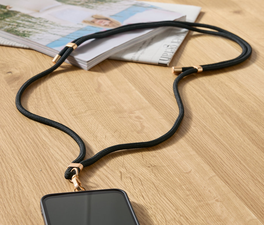 Egy fekete telefontok arany részletekkel egy asztalon fekszik egy magazin és egy bézs kézitáska mellett.
