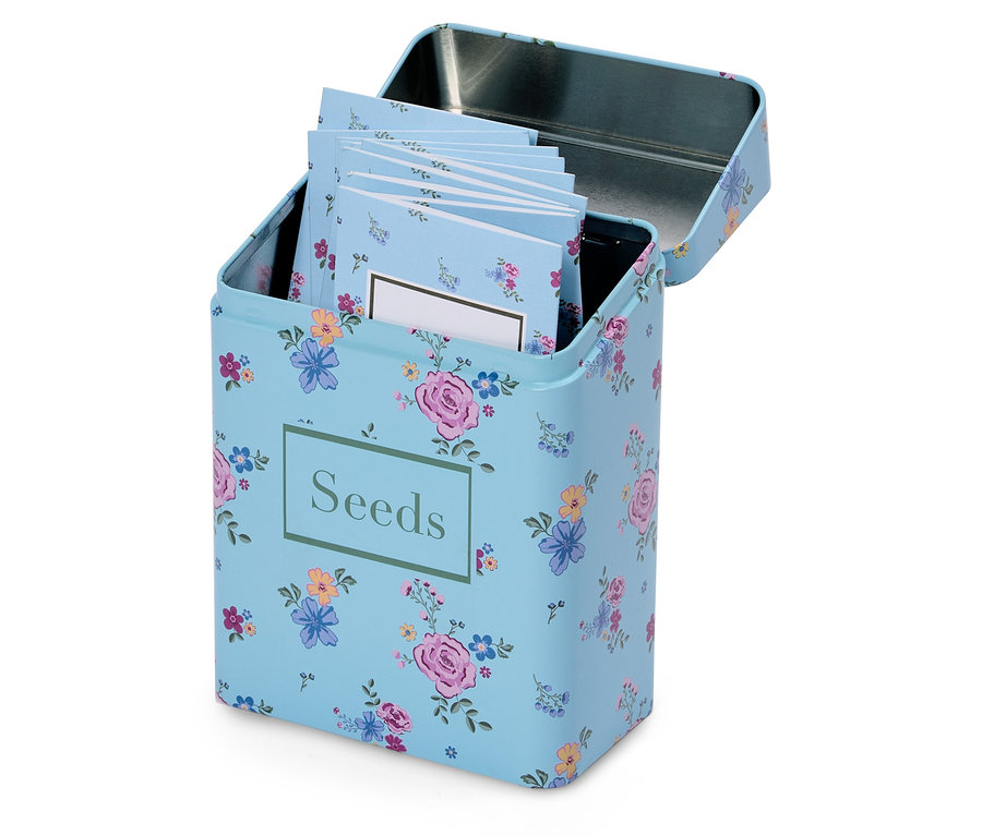 Egy nyitott, világoskék virágmintás magtároló doboz "Seeds" felirattal és több kis jegyzettömbbel a belsejében.