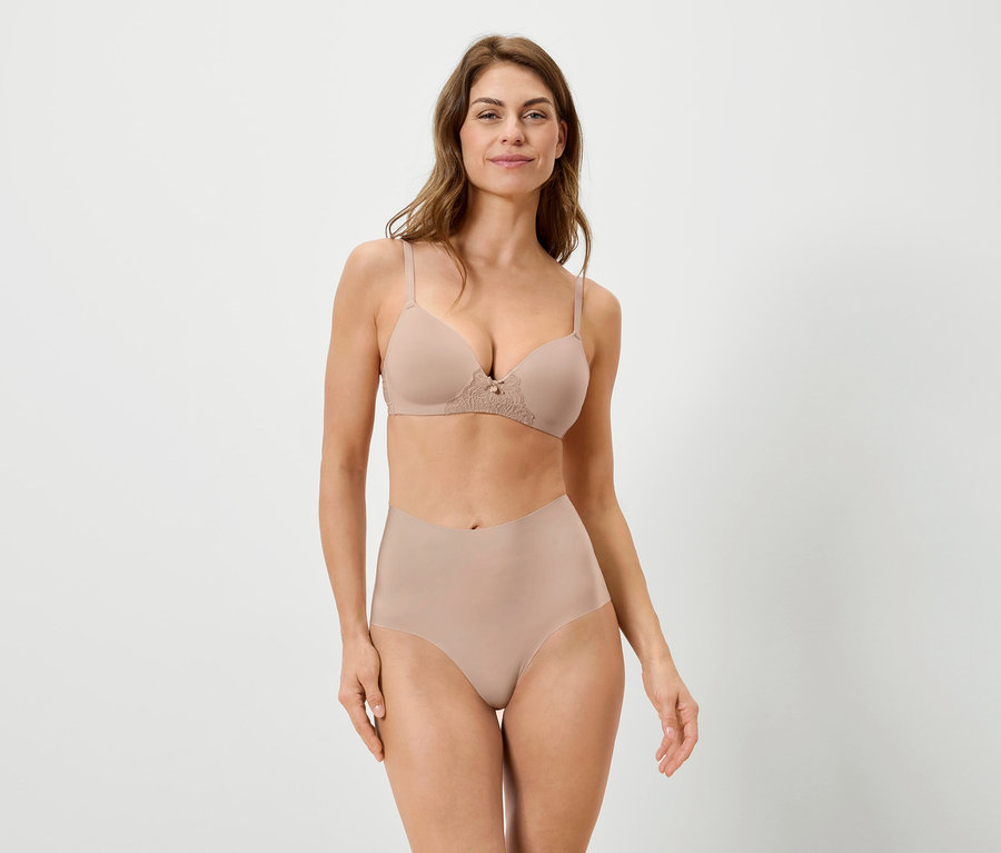 Nő visel testszínű melltartót és bugyit fehér háttér előtt.