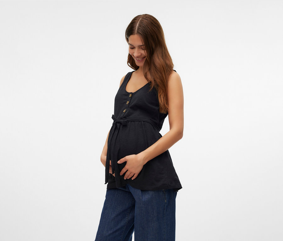 Egy nő fogja a hasát, fekete MAMALICIOUS »MLEVI LIA« szoptatós felsőt és bő farmert visel.