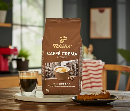 Egy csomag Caffè Crema Intense – 1 kg szemes kávé egy csésze kávé és egy szelet sütemény mellett.