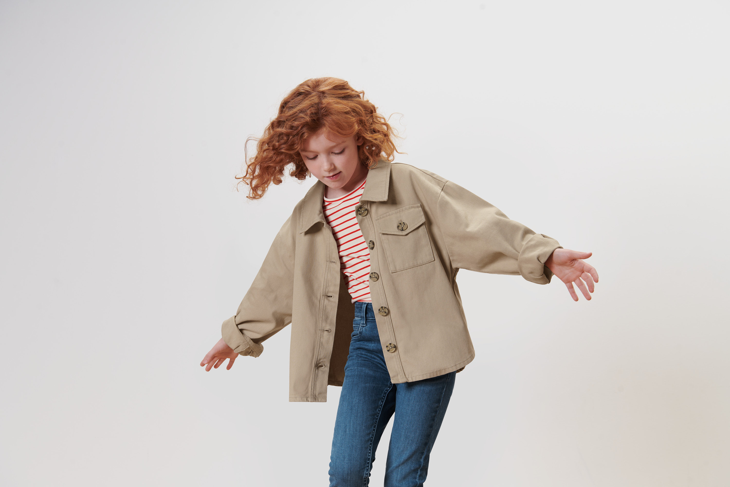 Vörös, göndör hajú lány integet a karjával, és egy bézs színű, lány oversize farmerdzsekit visel.