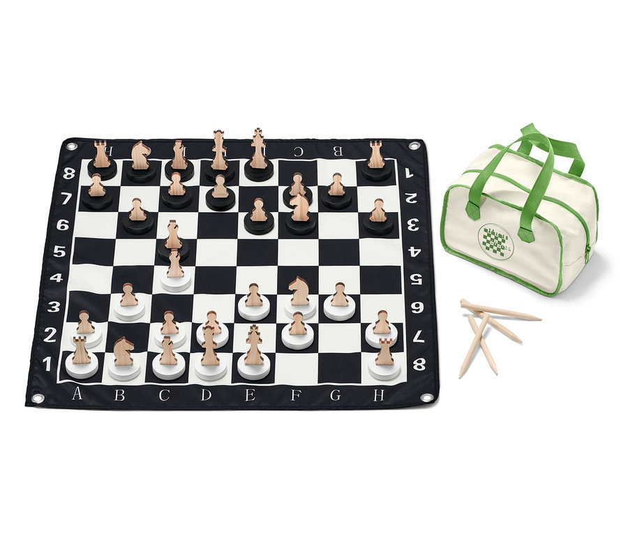 Egy XL-es sakkjáték van elrendezve egy fekete-fehér sakktáblán fa figurákkal, mellette egy táska.