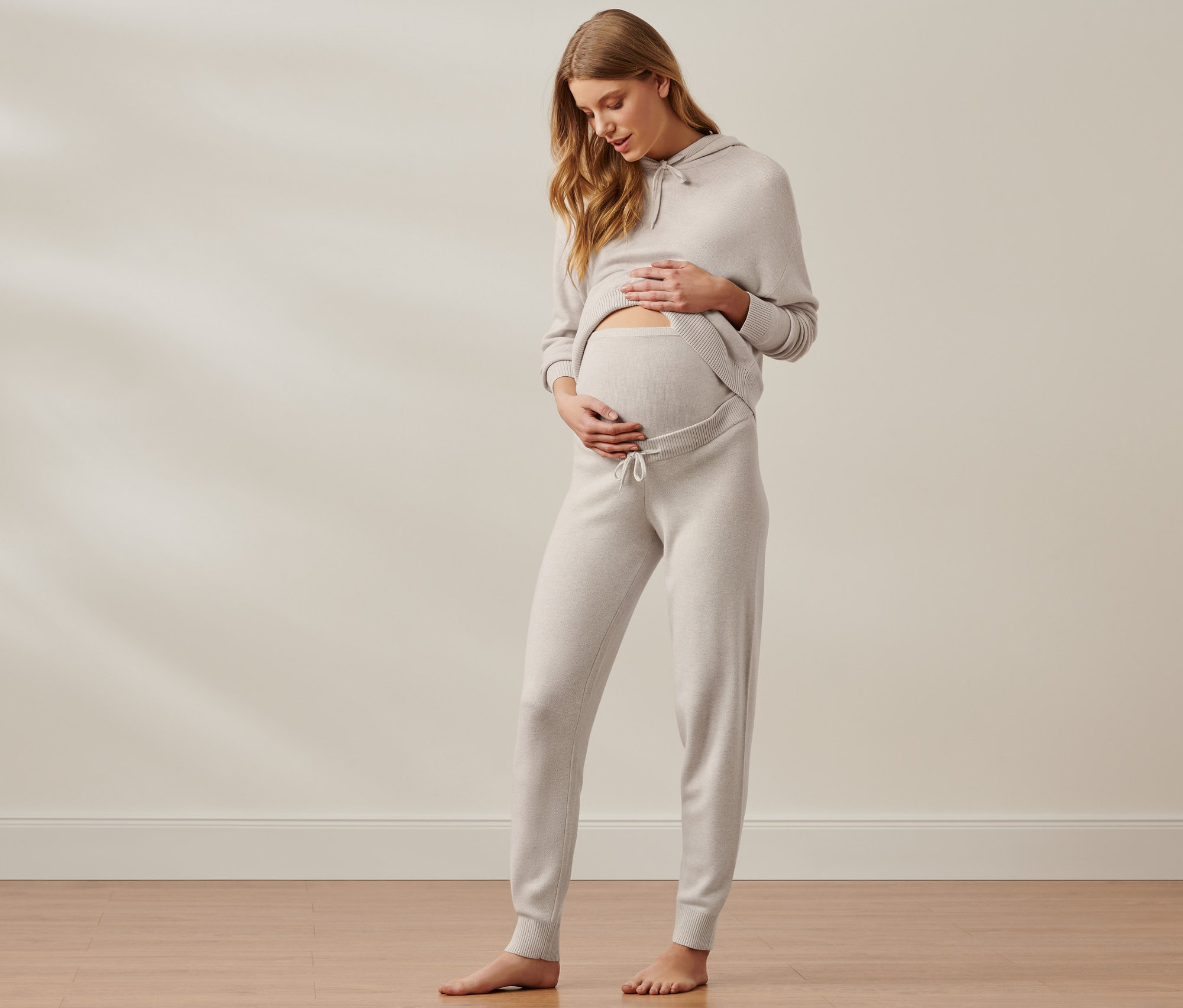 Kismama simogatja a hasát világosbarna kismama szabadidő szettben.