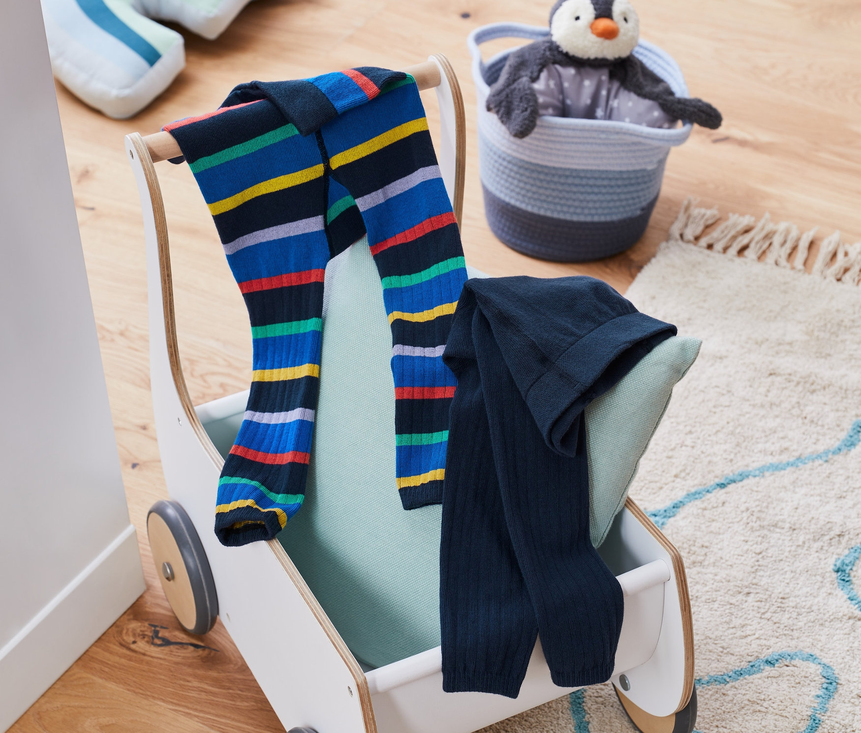 Két kötött leggings fekszik egy játékautón egy plüss pingvin mellett egy kosárban.