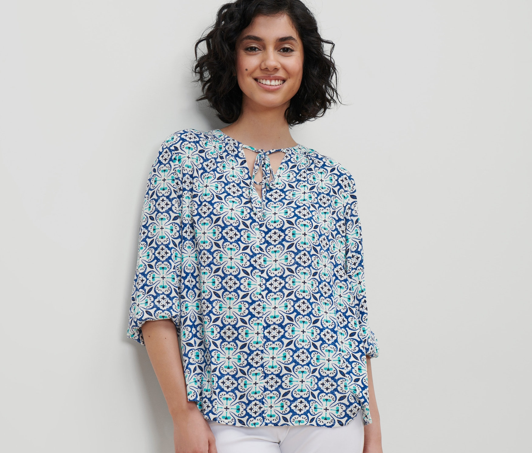 Nő visel mintás tunikablúzt és fehér nadrágot.