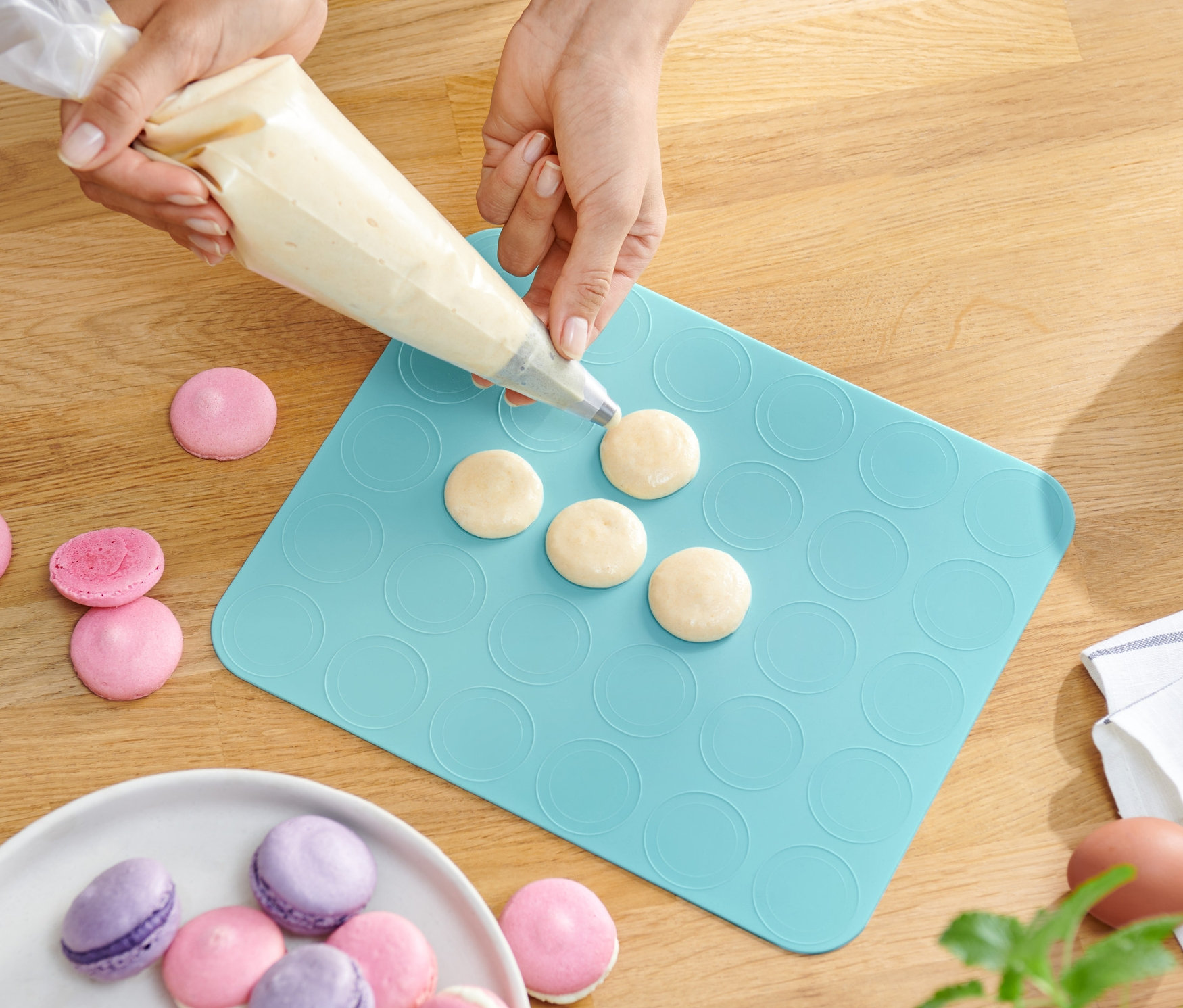 Egy személy tésztát tölt a szilikon macaron sütőlapra.