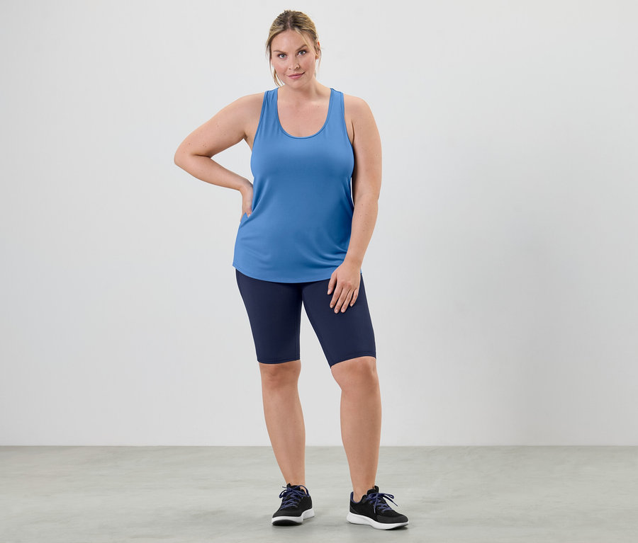 Egy nő egy kétrészes szett égszínkék funkcionális felsőjében és kerékpáros rövidnadrágban pózol.