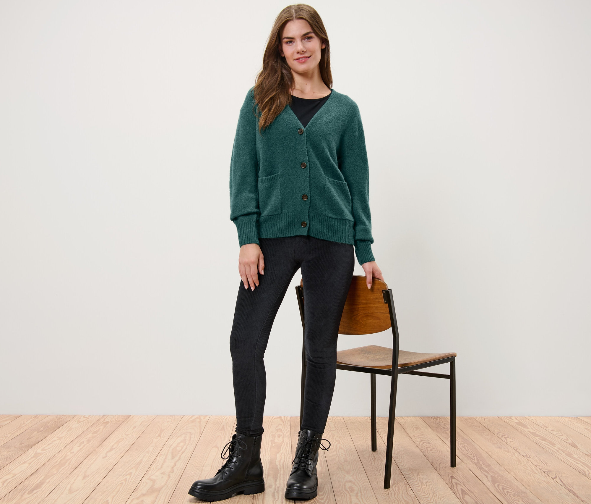 Nő áll, sötétzöld, gyapjú kötött kardigánt visel.