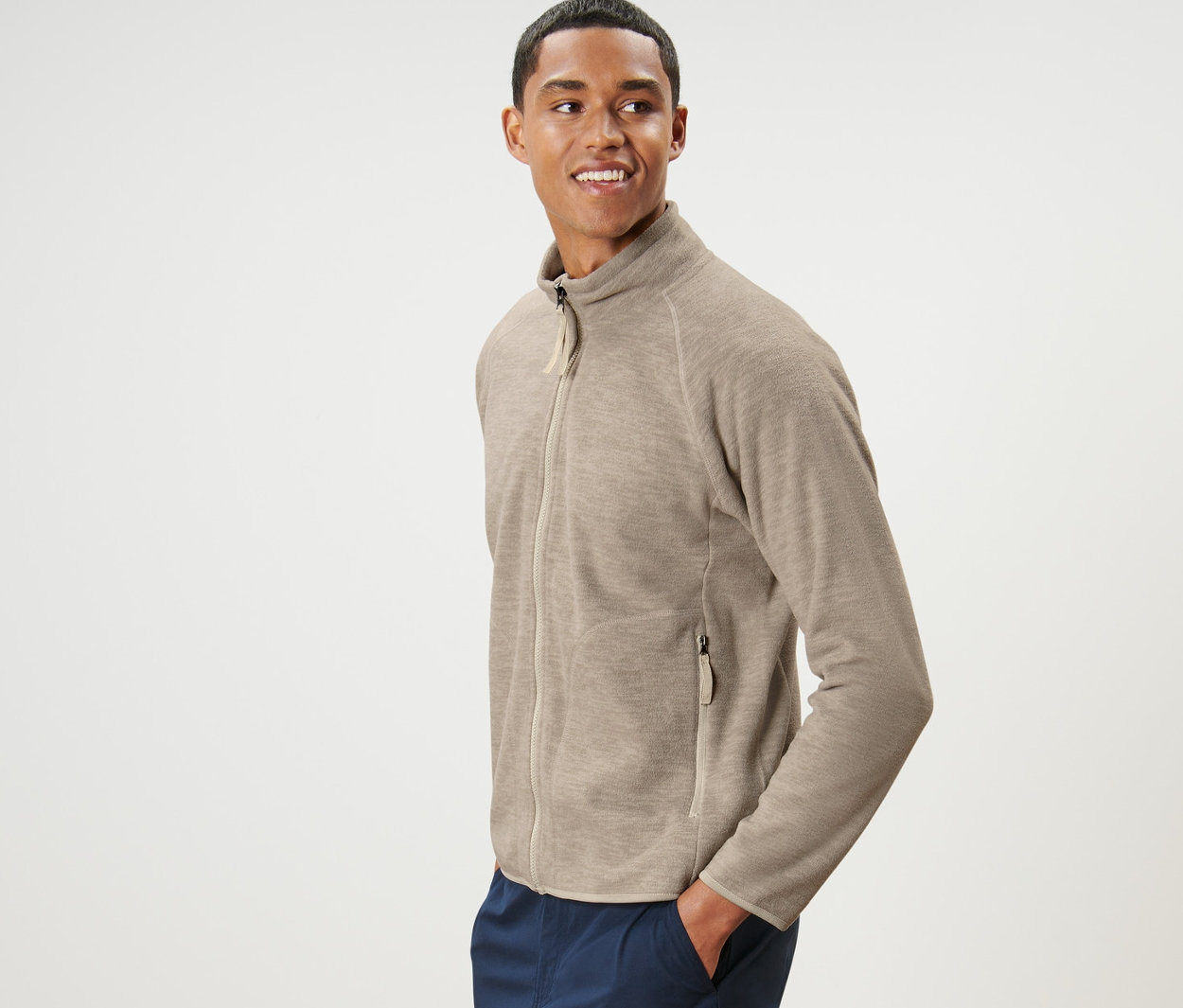 Férfi pózol bézs színű férfi polárfelsőben és sötétkék nadrágban.
