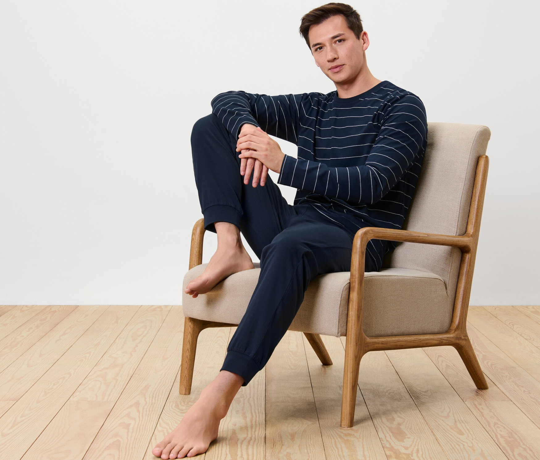 Férfi ül egy fotelben és sötétkék csíkos férfi jersey pizsamát visel.