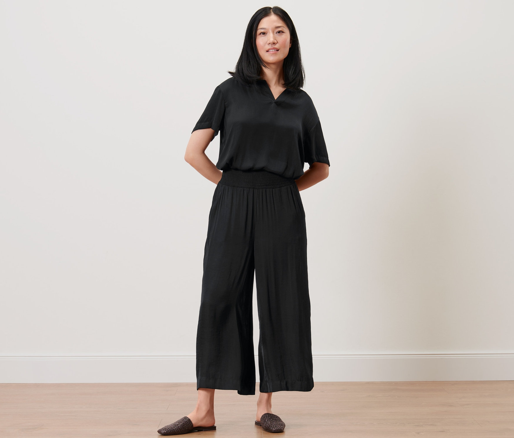 Nő pózol fekete, 3/4-es bőszárú nadrágban és felsőben.