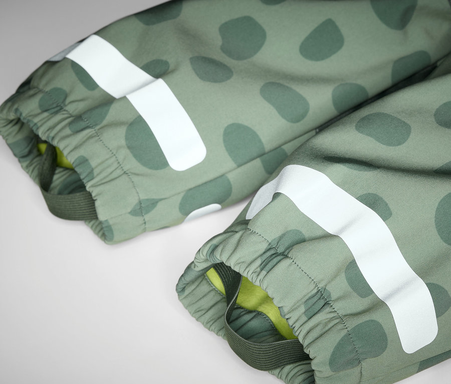 Egy olívazöld mintás, fehér fényvisszaverő csíkkal ellátott gyermek softshell kezeslábas részletének fotója.