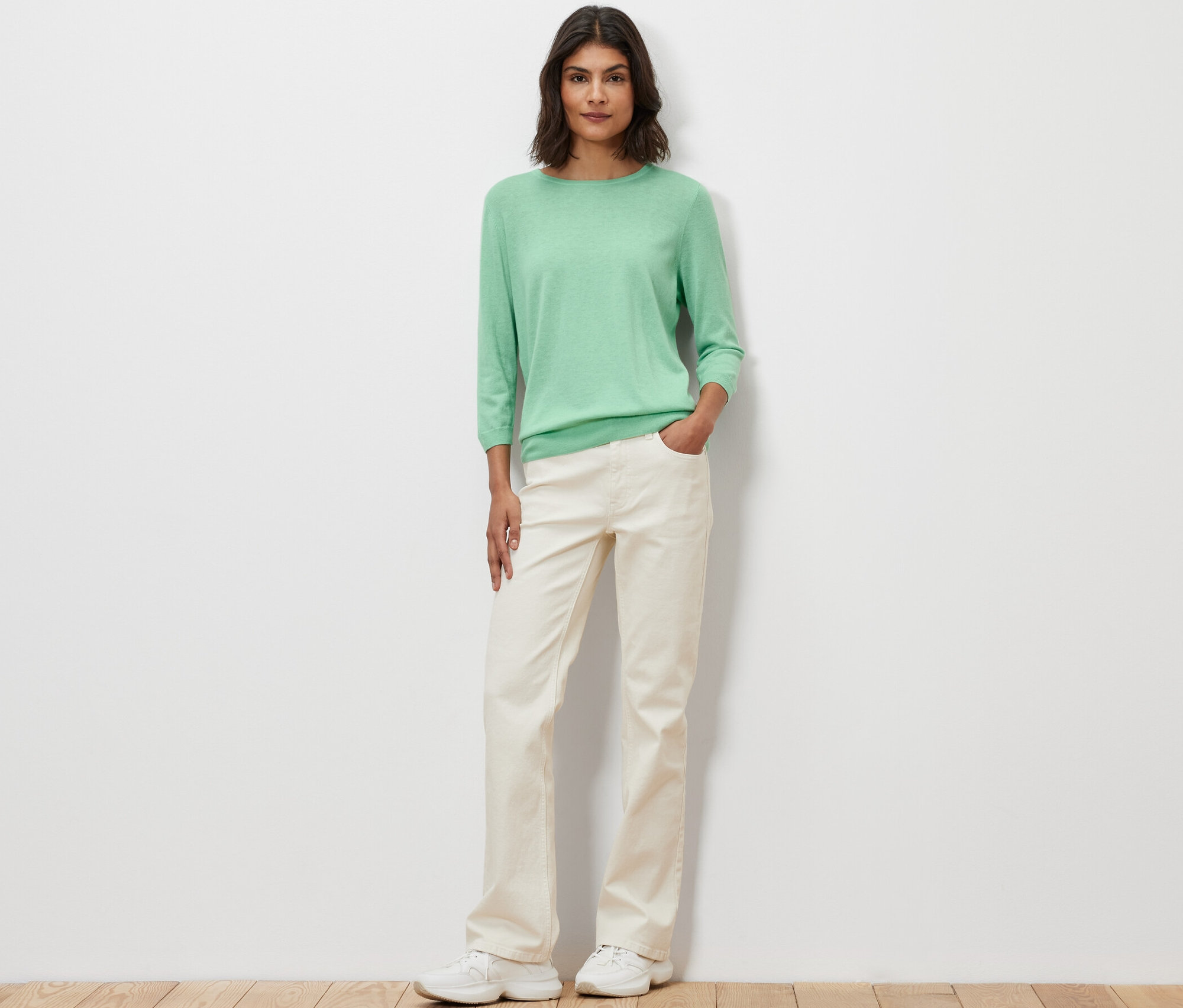 Egy nő pózol világoszöld, finomkötésű, selyemmel ellátott pulóvert viselve.