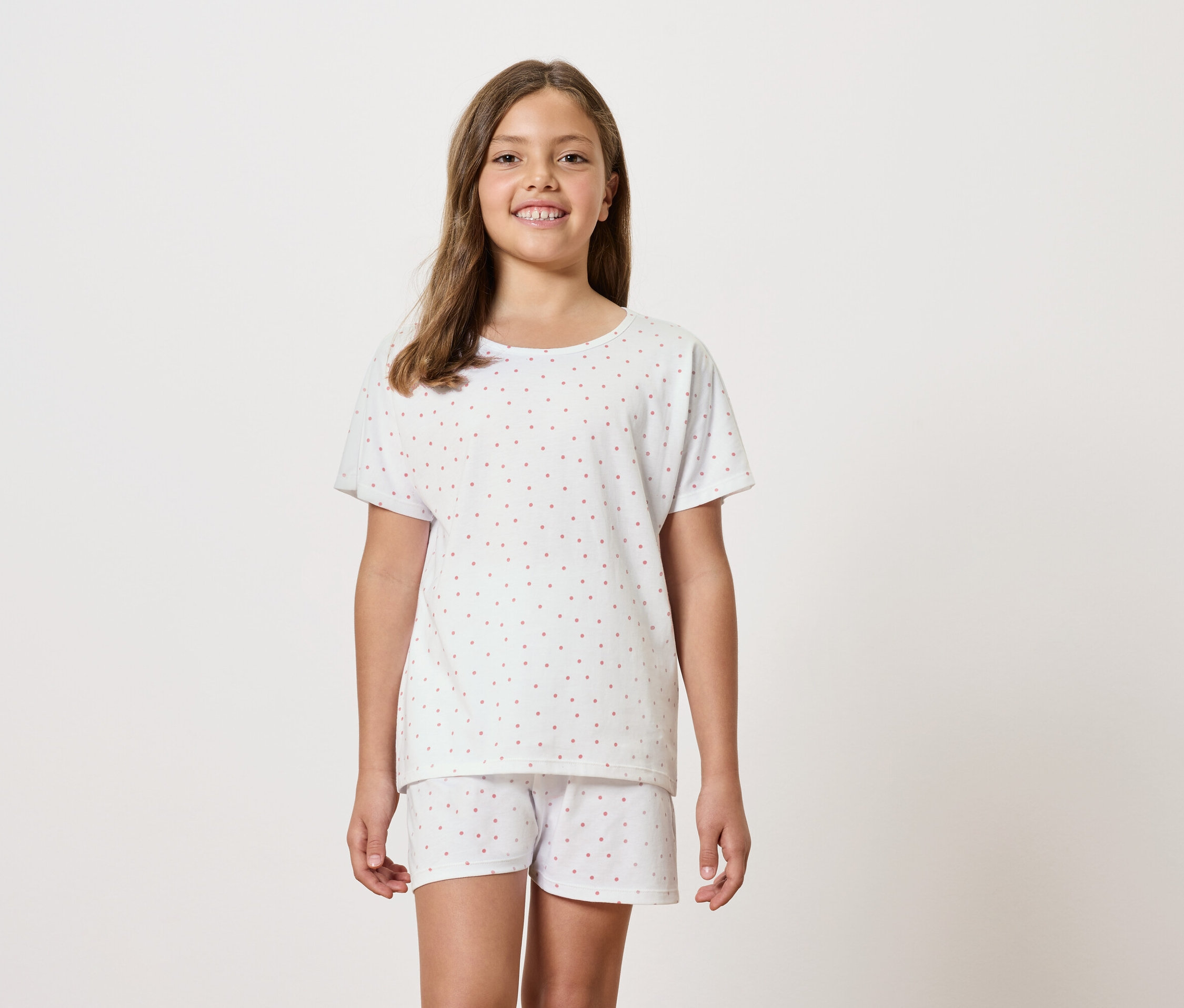Lány fehér, rövid ujjú pizsamát és rövidnadrágot visel.