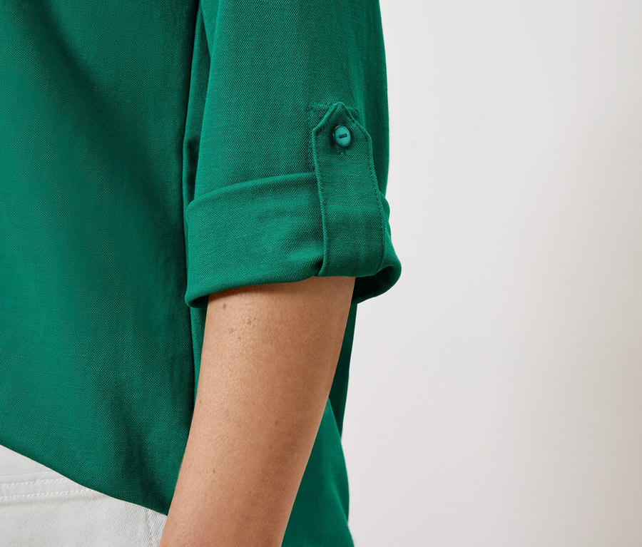 Egy női zöld ing részlete gombbal rögzített, felhajtott ujjakkal.