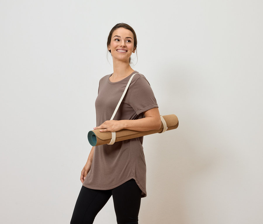 Mosolygó nő jógamatracot visz a vállán.