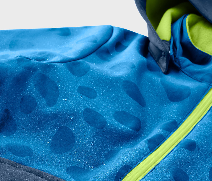 Kék gyerek softshell kabát részlete, mely esőben színt vált, zöld cipzárral.