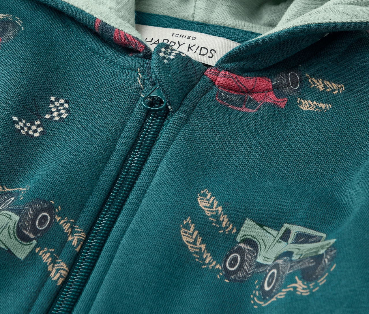 Egy zöld, cipzáras, autómintás gyerek pulóver részlete.