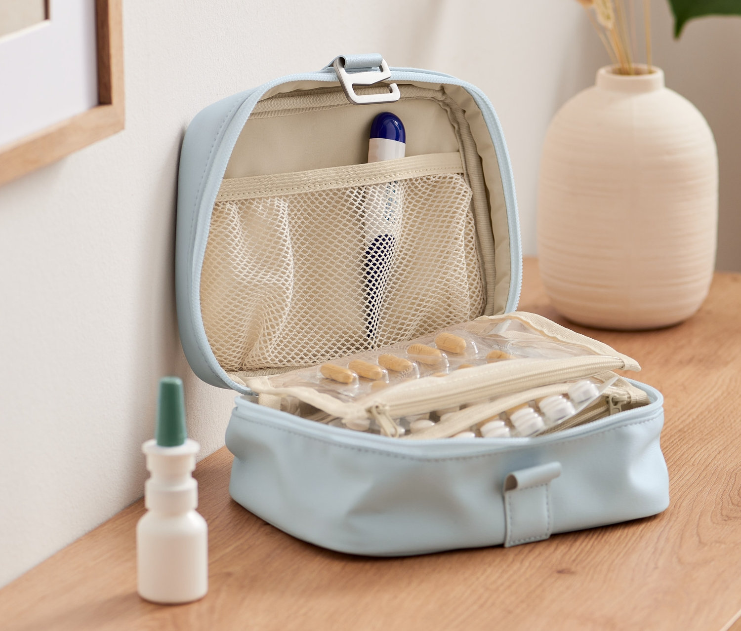 Nyitott, világoskék gyógyszeres táska gyógyszerekkel és fiolákkal egy fa asztalon.