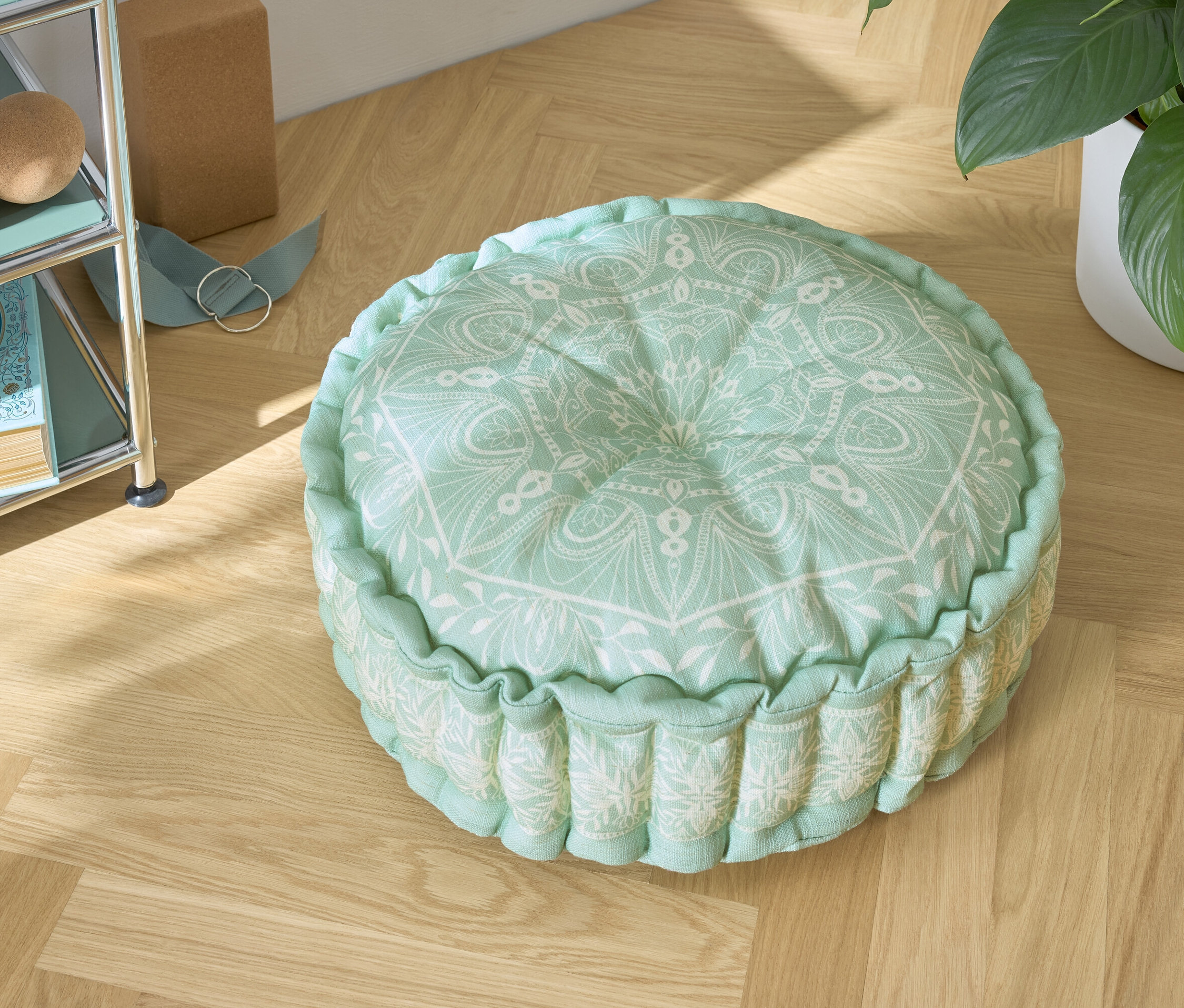 Zöld ülőpárna fehér mintával egy fa padlón.