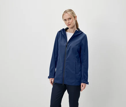Egy nő pózol sötétkék softshell kabátban, kapucnival és sötétkék nadrágban.