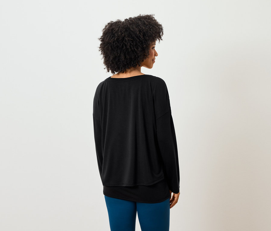 Hátulról látható egy göndör hajú nő, aki fekete hosszú ujjú felsőt és kék leggingst visel.