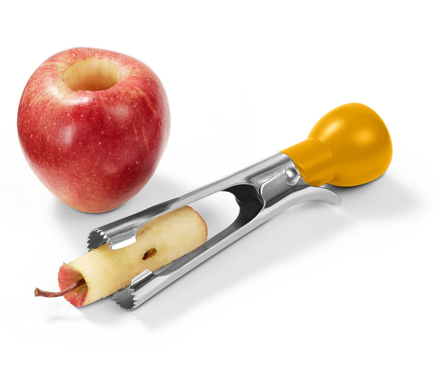 Egy piros alma kivájt közepével egy sárga nyelű rozsdamentes acél magozó mellett áll, amely egy második almából távolítja el a magot.