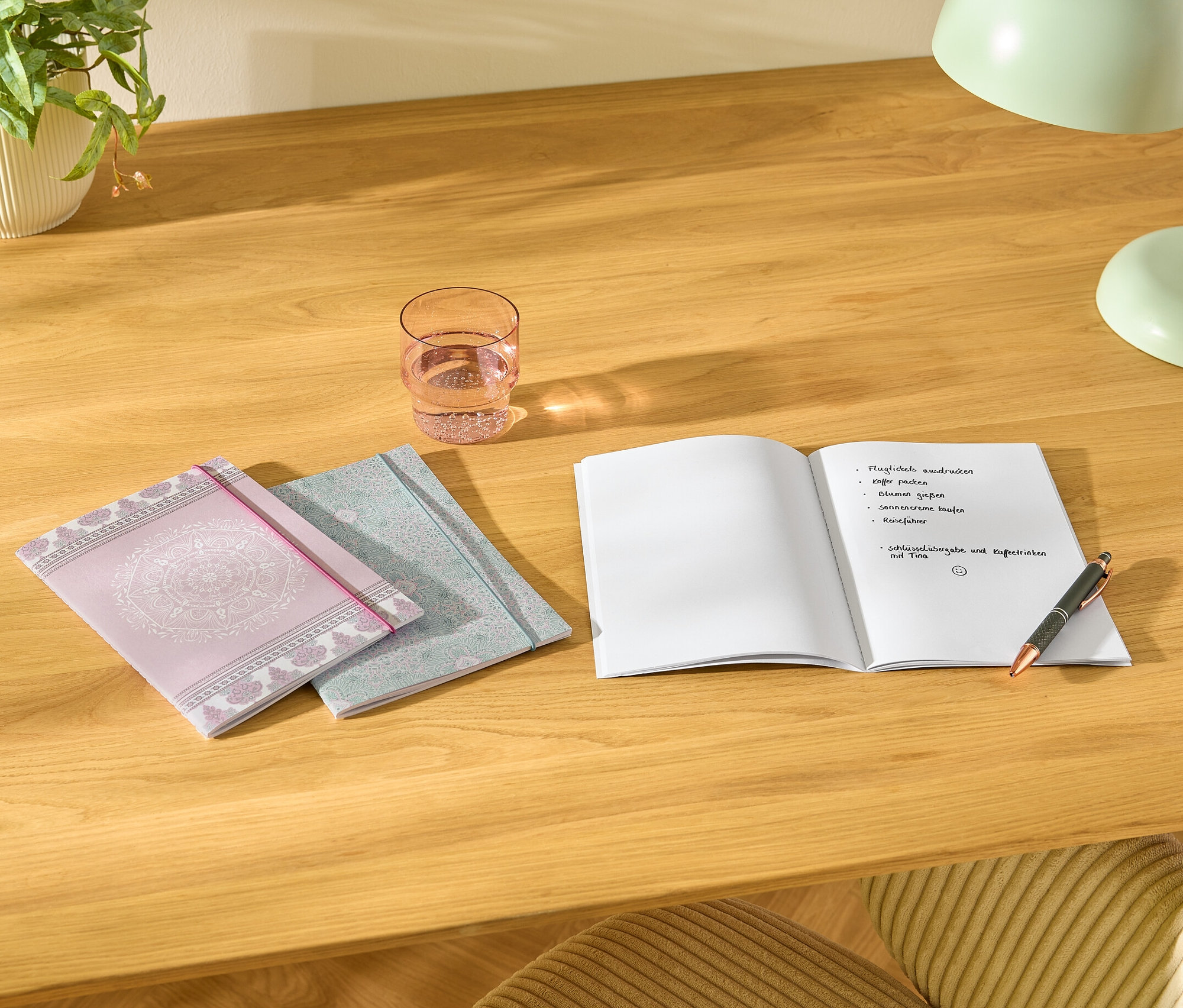 Egy asztalon három darab Notizbücher, egy pohár víz, egy nyitott jegyzetfüzet jegyzetekkel és egy toll.