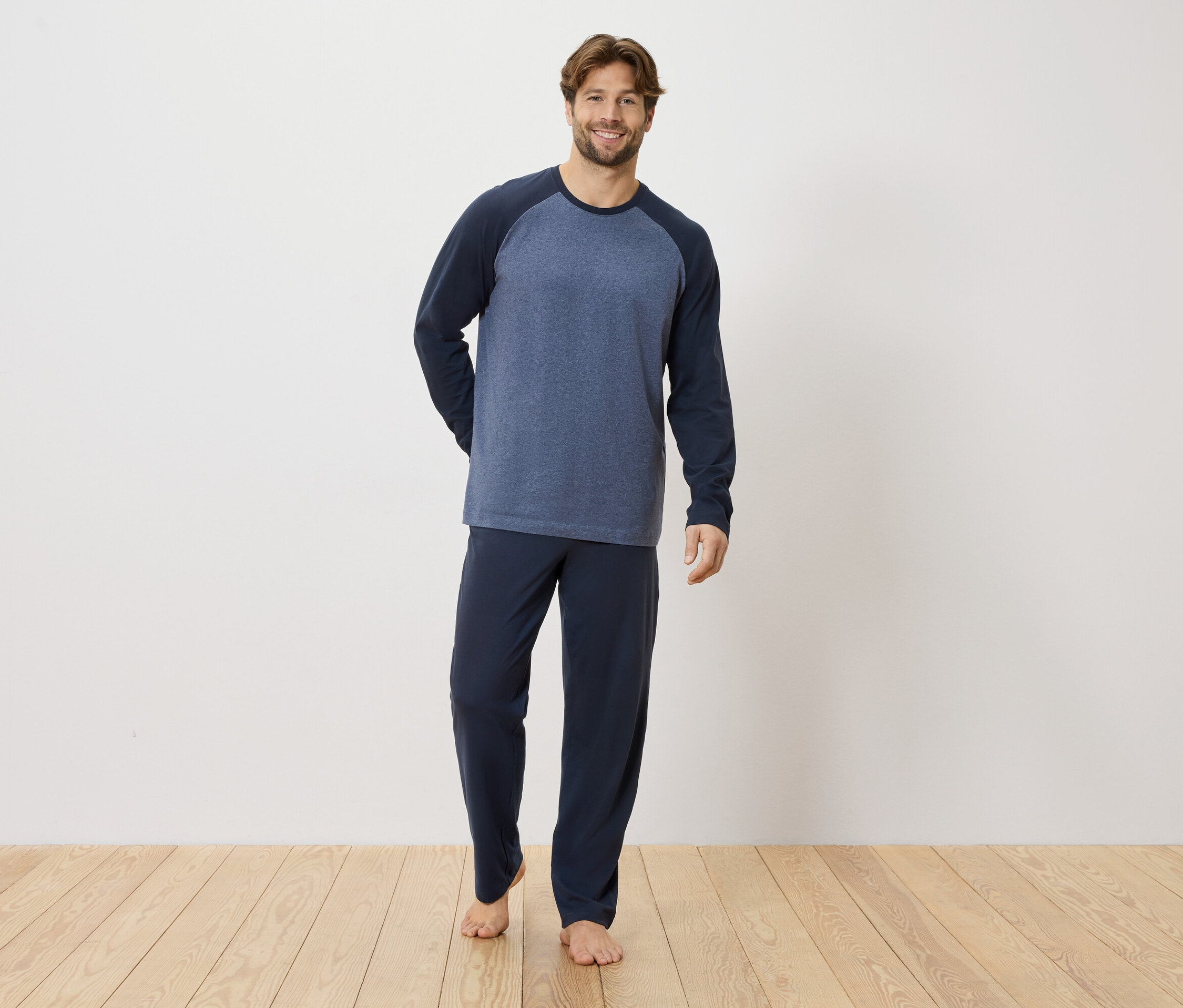 Férfi áll mezítláb a fapadlón, sötétkék pizsamában.