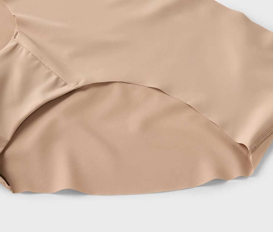 Egy bézs női alsónemű közeli képe világosszürke háttérrel.