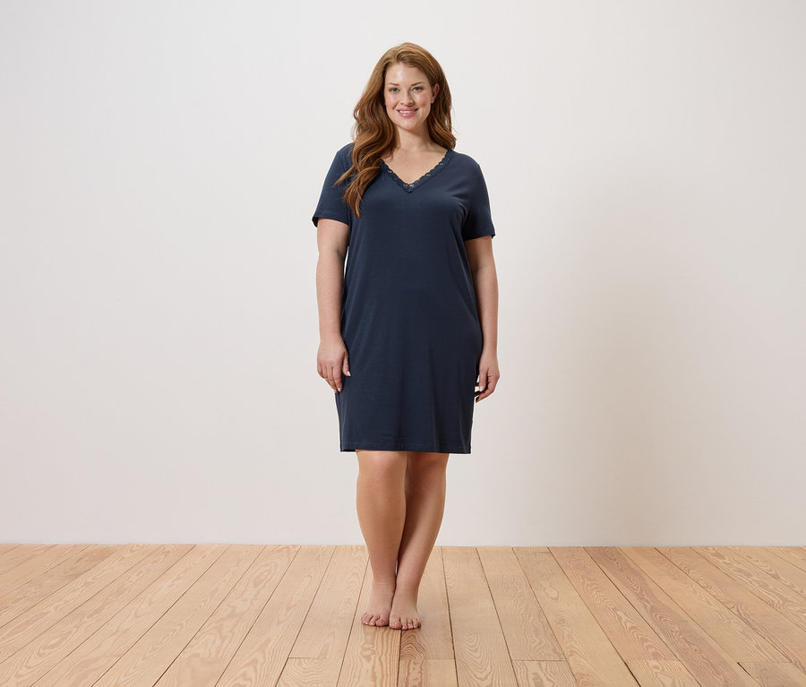 Nő áll mezítláb egy fapadlón, és egy sötétkék hálóinget visel.