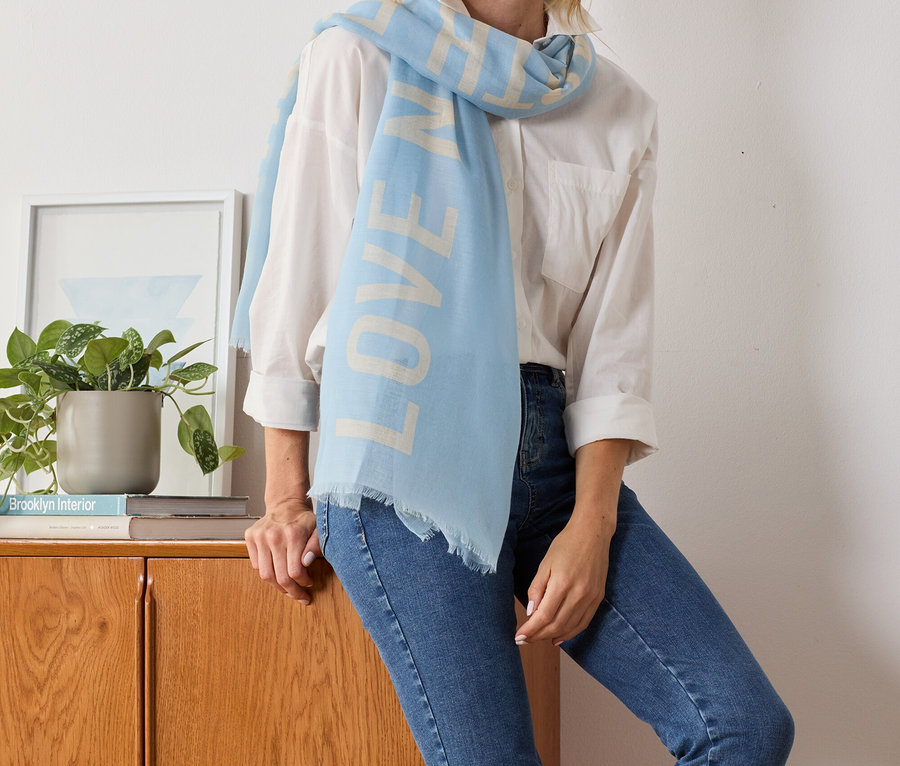 Egy szőke nő pózol egy világoskék, feliratos női szövetsálban.