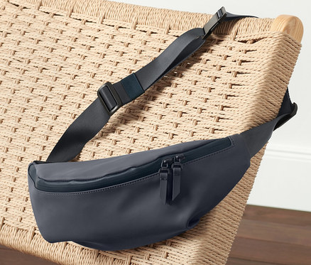 Egy sötétkék női övtáska fekszik egy fonott széken rózsaszín sportruházat mellett.