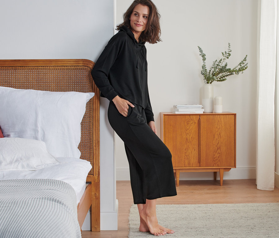 Nő dől az ágynak fekete 7/8-os szabadidő szettben.