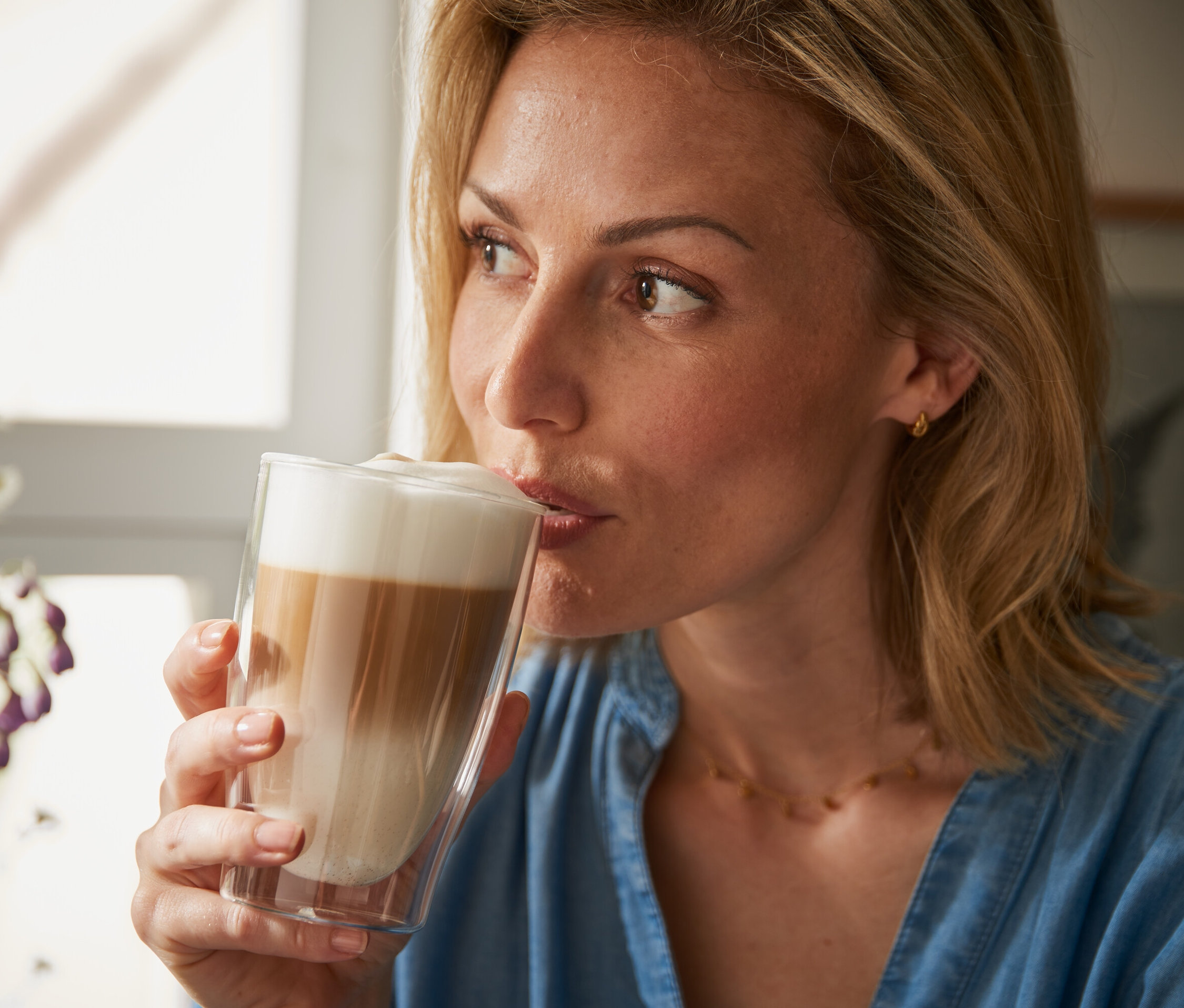 Nő iszik egy latte macchiatót egy duplafalú pohárból.