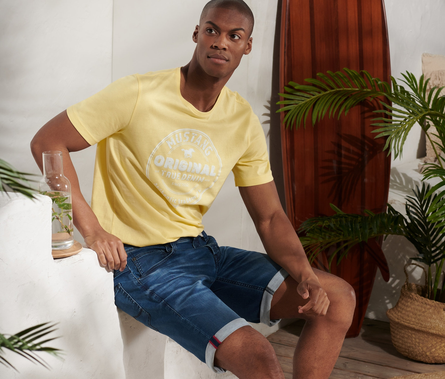 Férfi ül és kék Mustang farmer rövidnadrágot és sárga pólót visel.