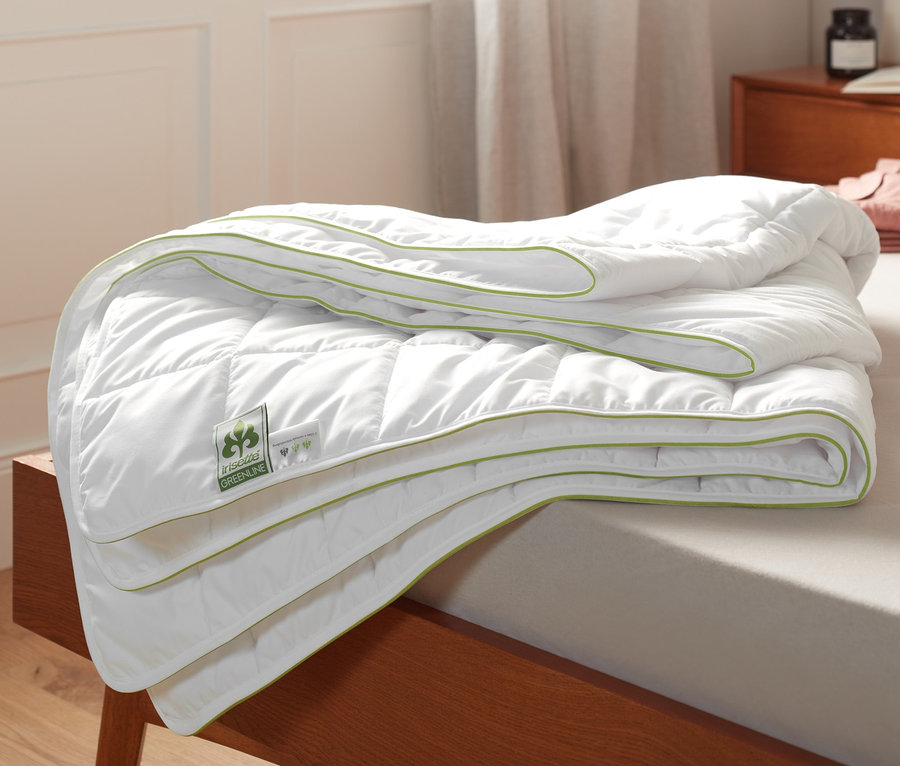 Egy összehajtott, fehér irisette® greenline relaxációs súlyozott takaró zöld szegéllyel egy ágyon.