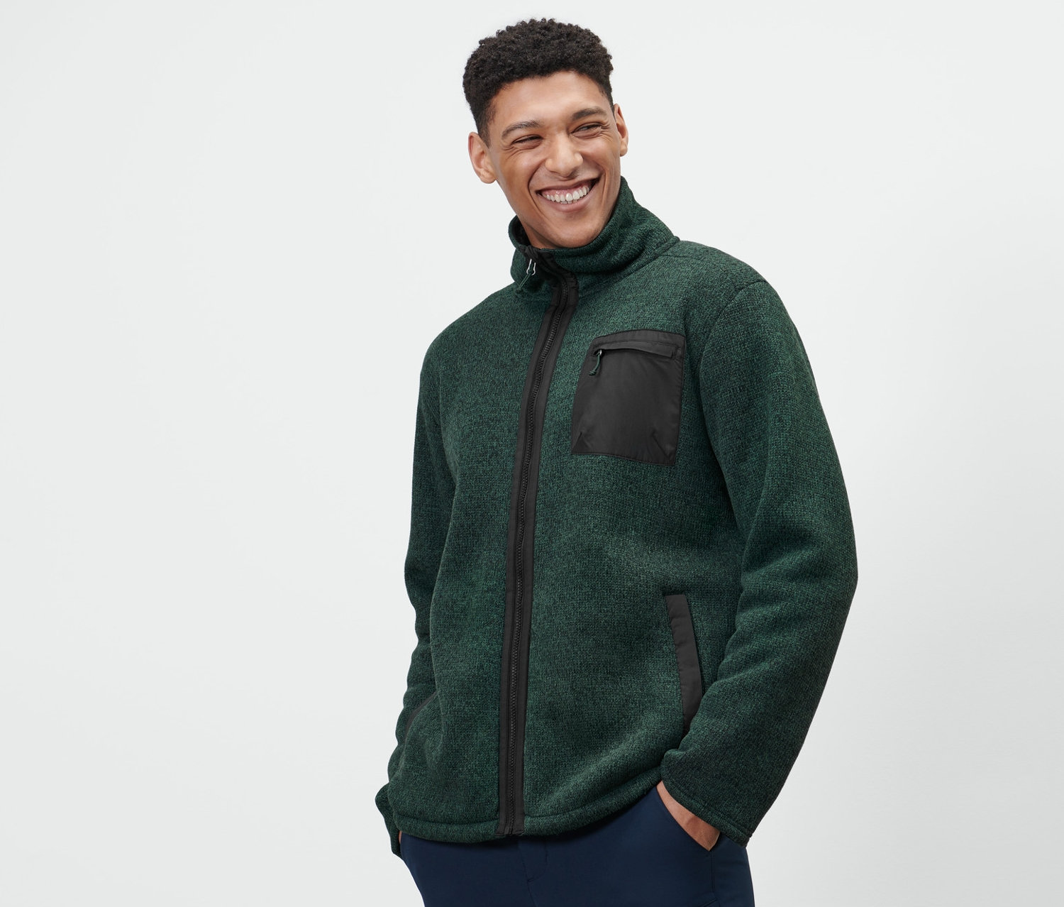 Egy férfi zöld kötött termo polárfelsőt és sötétkék nadrágot visel.