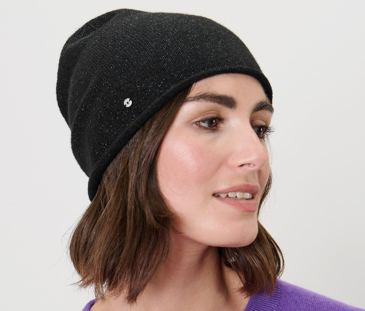 Barna hajú nő visel egy fekete, csillogó finomkötésű sapkát.