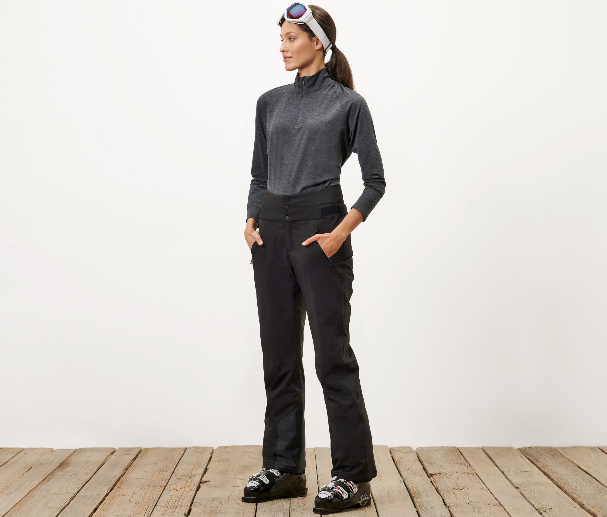 Egy nő áll, kezével a fekete, magas derekú sínadrágja zsebében.