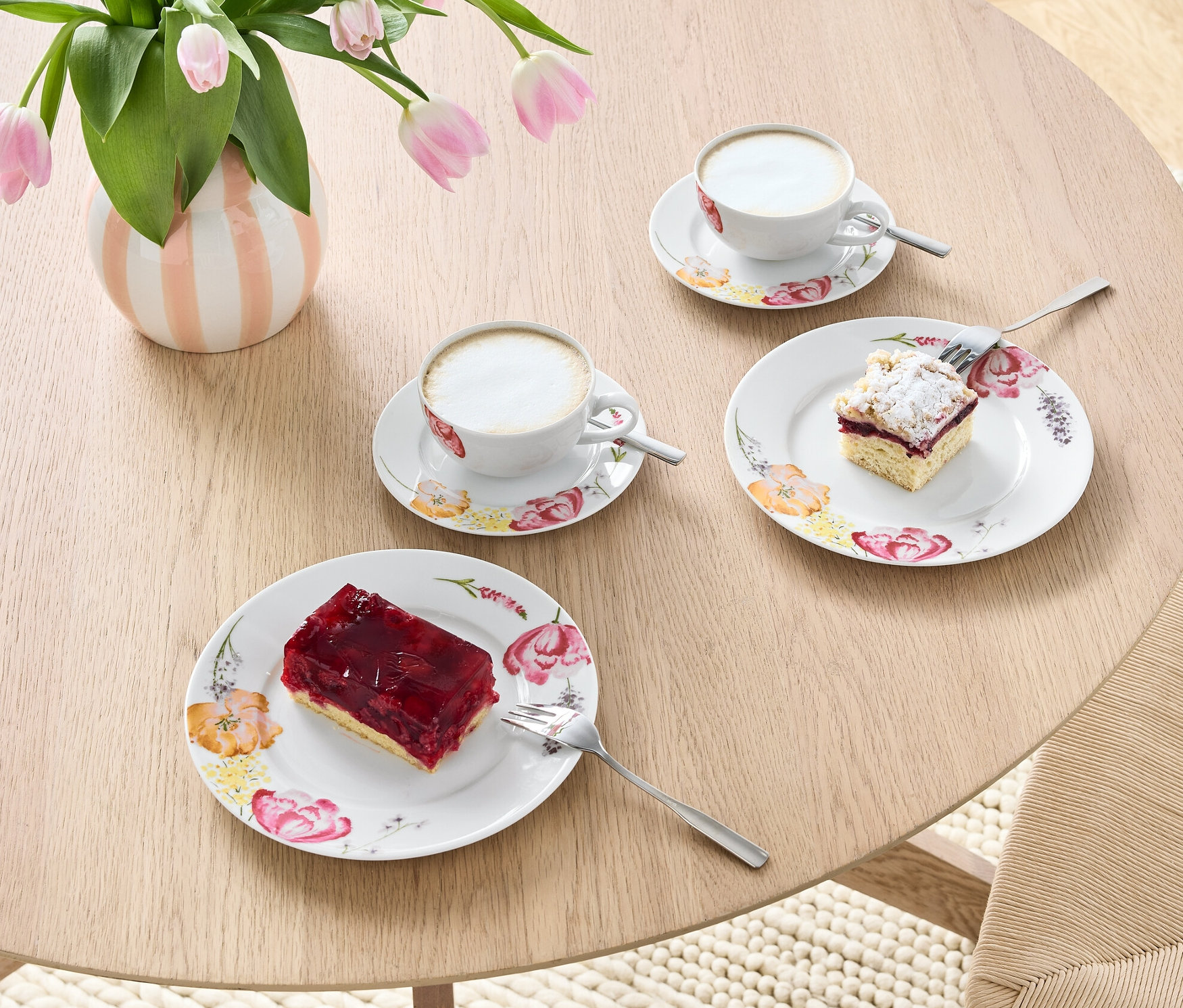 Egy asztalon egy váza tulipánnal és egy 6 részes porcelán kávéskészlet kávéval és süteményekkel.