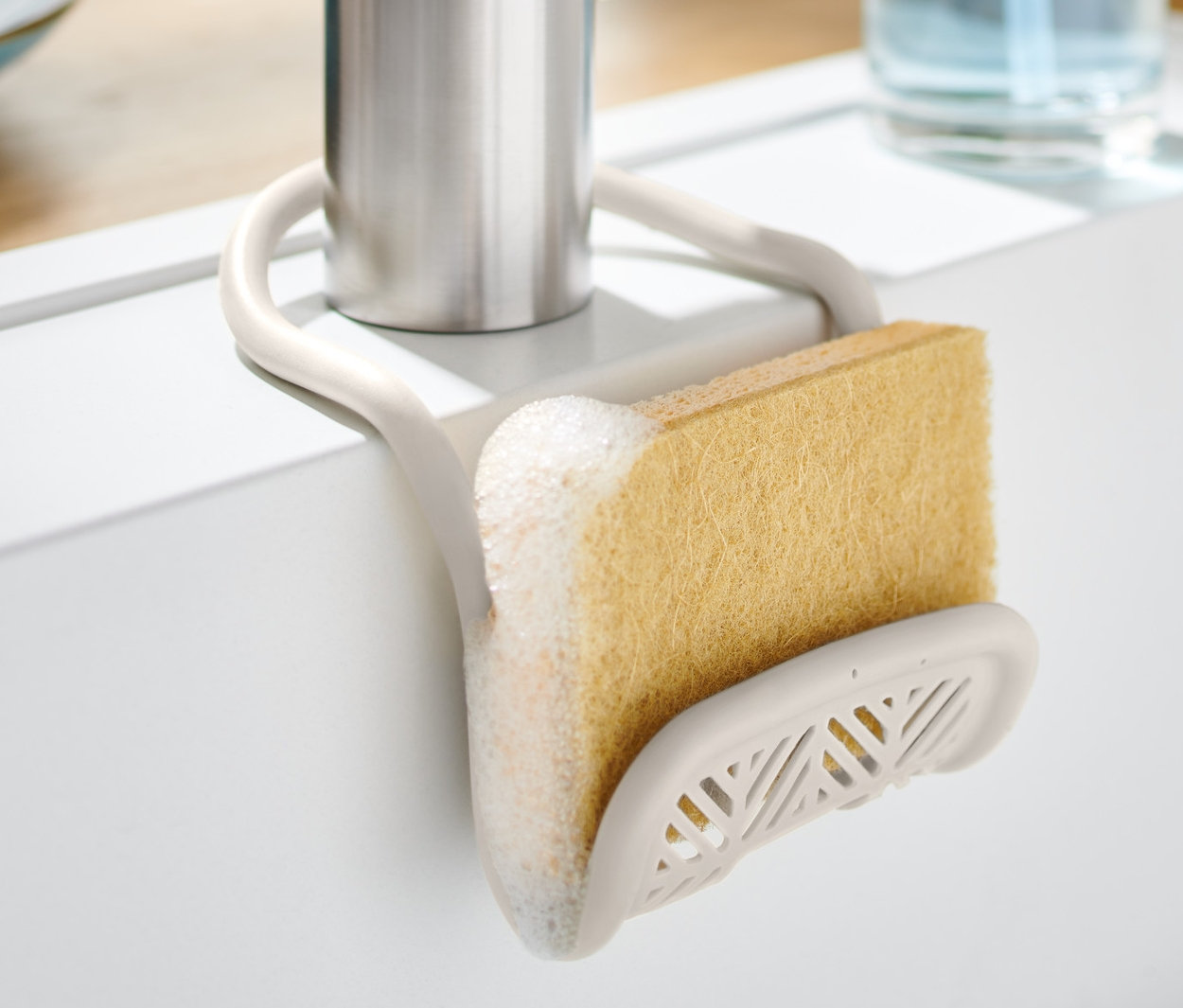 Szivacstartó szivaccsal egy csaptelepre szerelve egy fehér mosogatótálcában.