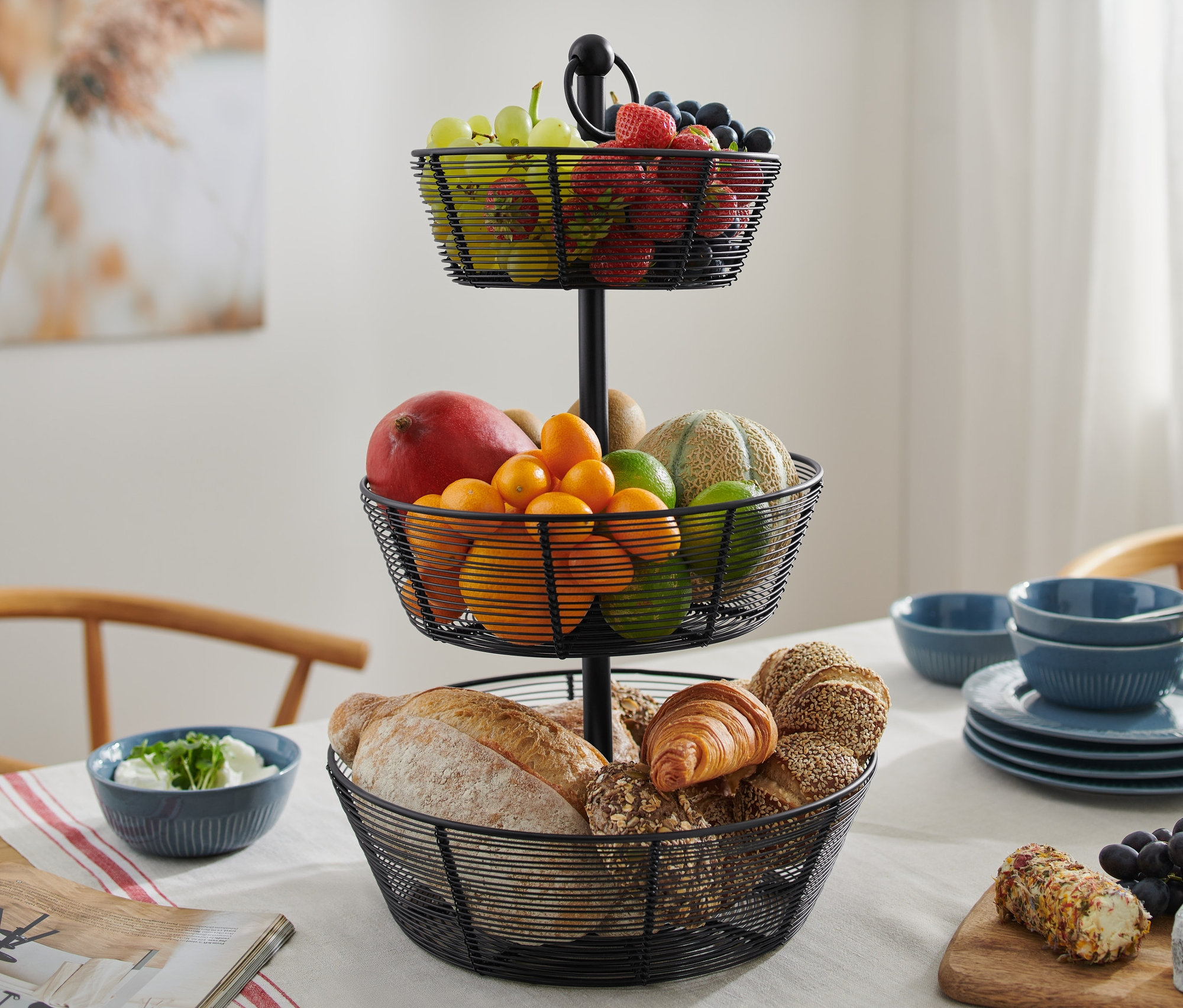 Egy háromszintes, fekete fém emeletes kínáló gyümölcsökkel és péksüteményekkel az asztalon.