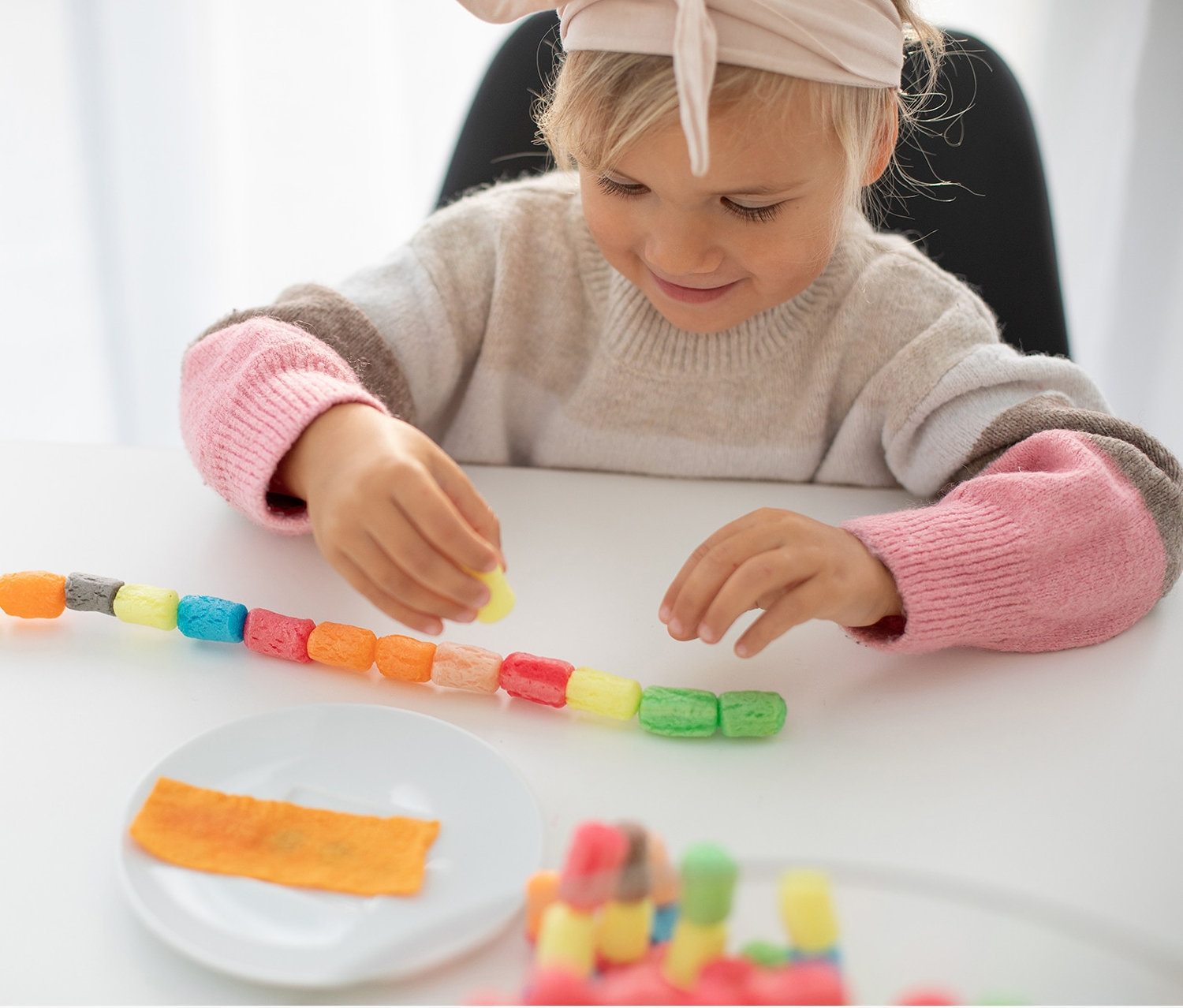 Egy kislány PlayMais®-szettel játszik, és színes láncot készít egy fehér asztalon.