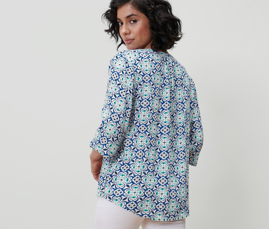 Egy nő visszanéz a válla fölött, nyomott mintás tunikablúzt visel.