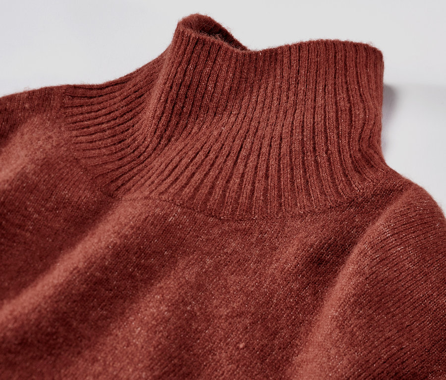 Egy rozsdabarna, gyapjú tartalmú kötött ruha részlete, garbó nyakkal.