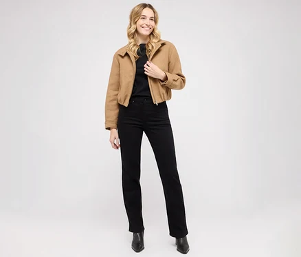 Nő pózol Angels denim »Lara« straight fit farmernadrágban, fekete felsőben és barna dzsekiben.