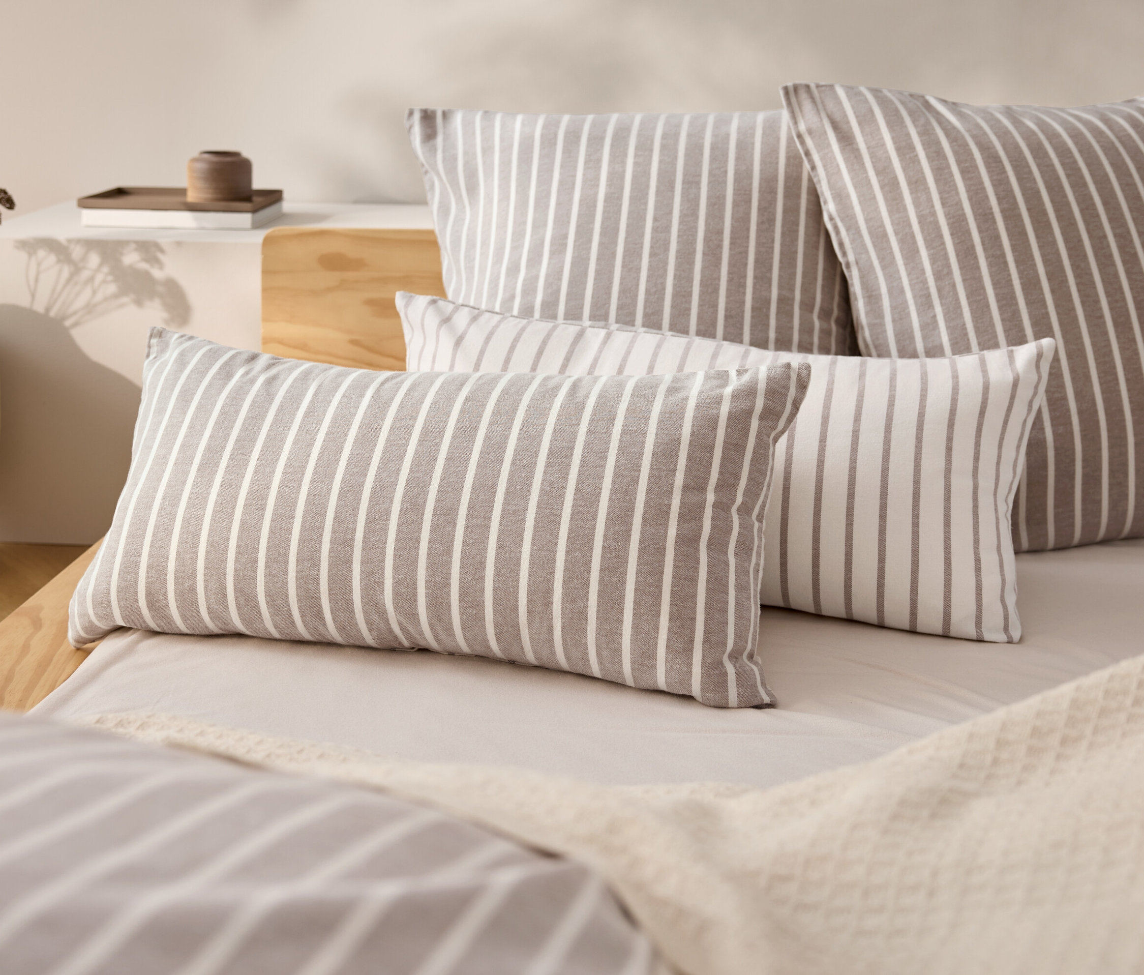 Négy csíkos párna egy ágyon bézs színű ágytakaróval.