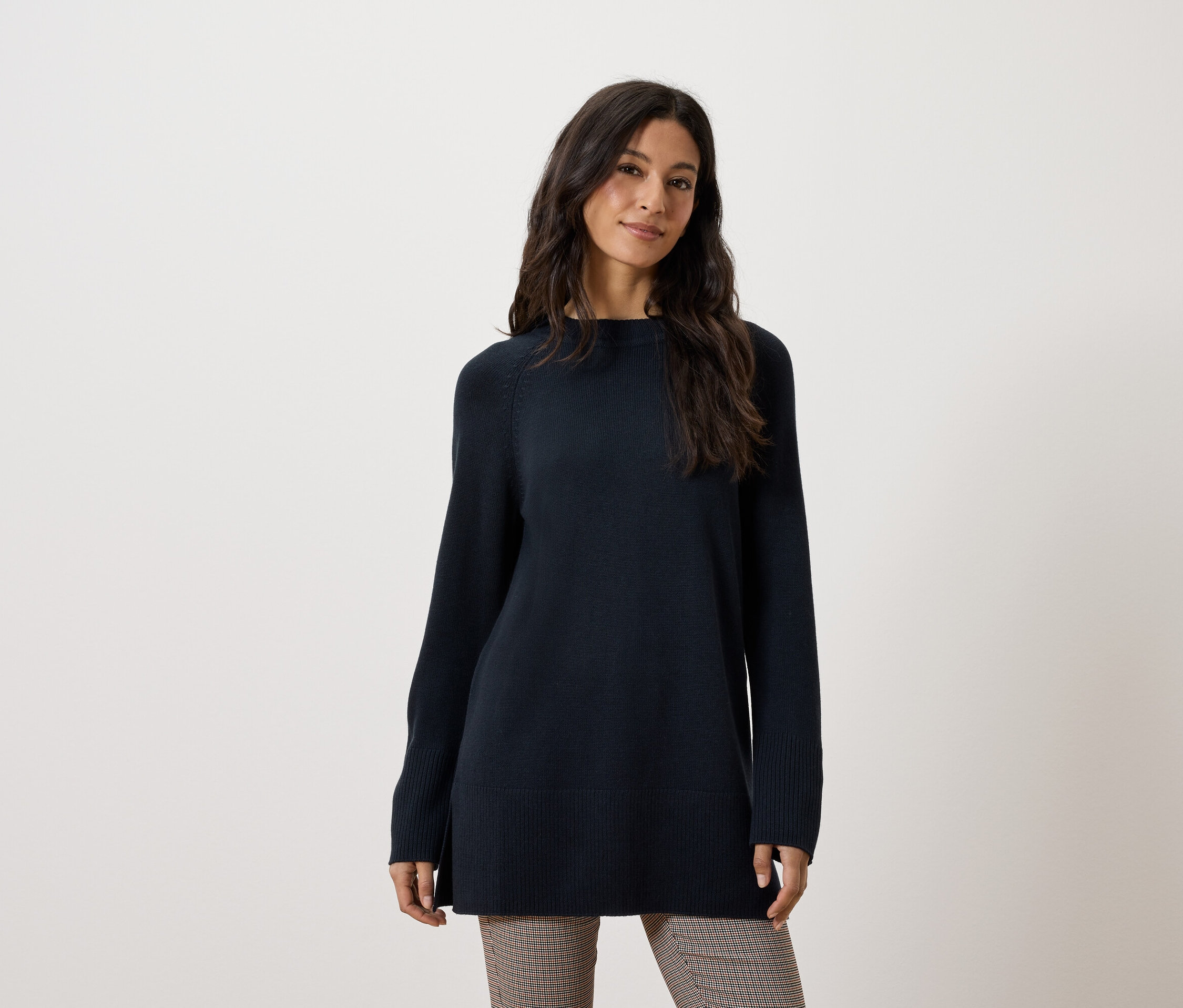 Egy nő hosszú, sötétkék pulóvert és barna nadrágot visel.